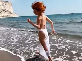 Sexy red-haired girl enjoys a walk by the sea